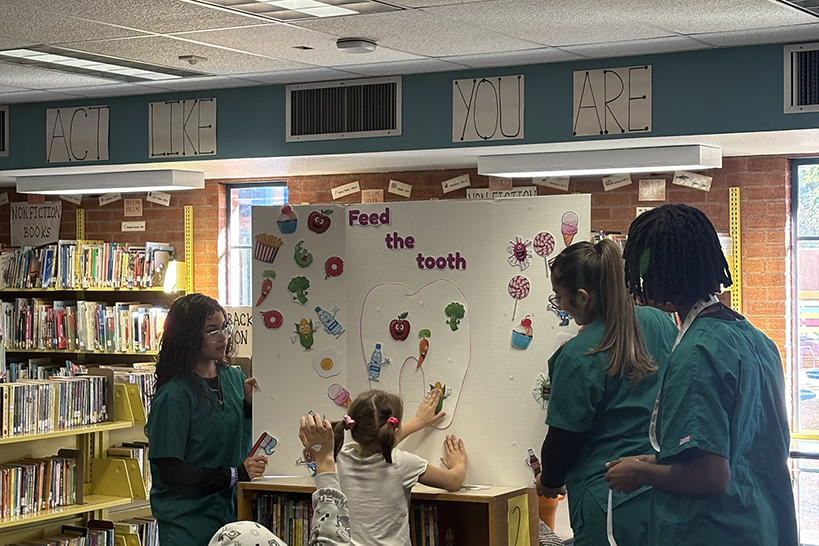 A girl puts a cutout of a vegetable on a poster image of a tooth