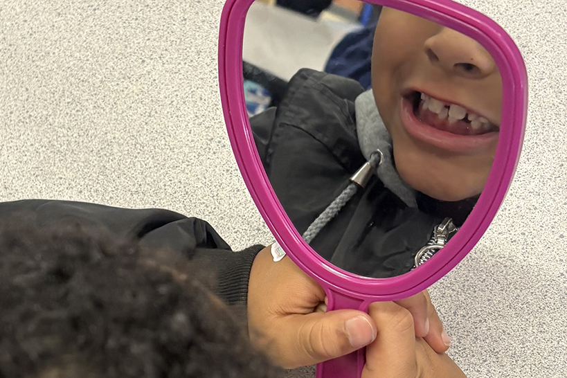 A girl looks at her teeth in a pink handheld mirror